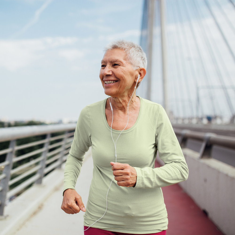 Hip replacement female patient jogging on a bridge with earphones, smiling as she preps for her surgery.