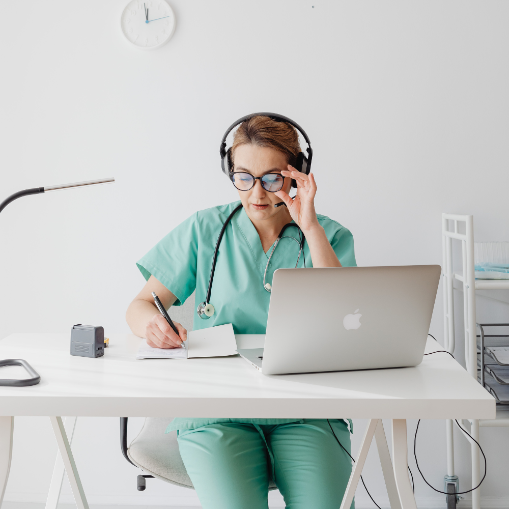 SurgicalRx surgery prep coach in green scrubs with headphones and a laptop at a desk.